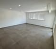 Large open room with gray tile flooring, white walls, and recessed lighting. The room has a clean, modern aesthetic.