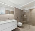 modern bathroom with white tiles, illuminated mirror, glass walk-in shower, white sink, white toilet