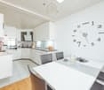 Modern kitchen with white cabinets, tiled floor, integrated appliances, dining table, clock