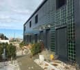 black building with solar panels on the exterior wall, entrance with awning, landscaped garden with plants and gravel path