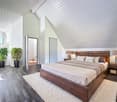 wooden bed, large window, wooden floor, lamps, white rug, nightstands, pillows, plants