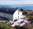 Modern white house, black roof, large windows, outdoor dining area, small pool, garden, sea view