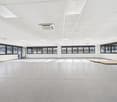 Empty room with white ceiling, white walls, large windows, tiled floor, and an open door.
