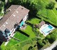 2 story house, brown roof, white walls, swimming pool, garden, green grass, trees