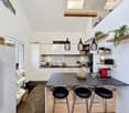 modern kitchen with white cabinets, black countertops, hanging lamps, kitchen island with stools, refrigerator, plants on shelves, skylight