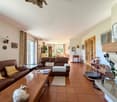 Cozy living room with brown leather sofas, wooden coffee table, tiled floor, fireplace, decorative items, wall lamps, glass windows, and framed pictures.