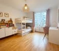 child's bedroom with wooden floor, bunk beds, white furniture, pink desk chairs, window with curtains, light fixture
