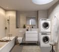 Spacious bathroom with modern design, featuring a vanity unit with sink, a toilet, a bathtub, and a stacked washer and dryer unit. The room has a large skylight and is tiled with neutral-colored tiles. There are also some decorative elements like plants a