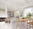 modern kitchen with fireplace, dining area with table and chairs, wooden floor, white walls, large windows