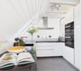 modern kitchen with white cabinets, black countertops, stainless steel appliances, open book on countertop, plants on window sill