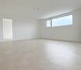 Spacious room with white walls, large windows, and a tiled floor. The room appears to be empty, providing a clean and minimalist look.