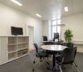modern office with white walls, gray carpet, round table, black chairs, white cabinet, desk, computer monitors, potted plant