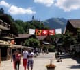 Street with four people walking, mountains in the background, three flags hanging between street lamps