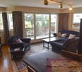 Spacious living room with large windows overlooking a balcony, hardwood floors, dark sofas, coffee table, and decorative pillows