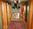 A hallway with wooden doors and green walls, oriental rug, picture frame on the wall, hats and other items on the wall