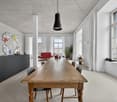 large room, long wooden table, black chairs, black cabinets, white walls, large windows, red couch in the other room