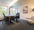 Office room with two desks, chairs, table, lamp, and window.