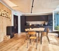 wooden cabinets, tiled floor, black table, chairs, kitchen appliances, wooden storage box, plant, wall with sign
