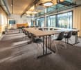 conference room with long wooden tables and black chairs, large windows, white walls, wooden floor, ceiling lights, whiteboards on the wall