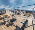 Wooden floor terrace with glass railings, modern seating, round tables, distant mountains and sky in the background