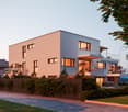 Modern 2-story house, white walls, multiple glass windows, balcony, wooden fence, driveway, parking, well-maintained lawn