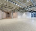 Large open commercial space with exposed concrete ceiling, ductwork, and lighting. The space has a tiled floor and appears to be a warehouse or industrial-style office area.