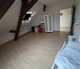 ample attic room with wooden beams, wooden floor, white walls, bed, desk, chair, wardrobe, open window, radiator