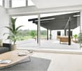 modern living room, gray couch, wooden coffee table, plants, large windows with glass sliding doors to a patio