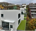 Modern white houses, green landscaped steps, multiple balconies, roof terrace with solar panels