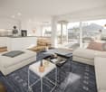 a modern living room with white kitchen, living and dining area, sliding glass doors leading to a terrace, hardwood floor, sliding doors, two round tables, and a rug