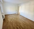 empty room with wooden floor, white walls, open door leading to another room