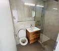 Modern bathroom with shower, toilet, sink, wooden cabinet, and mirror.