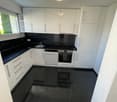 Modern kitchen with black tiled floor, white cabinets, and modern appliances. Kitchen features a sink, dishwasher, and oven.