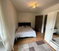 Bed with white blanket, rug, wardrobe, lamp, wooden floor