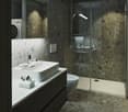 Modern bathroom with dark stone walls, white sink vanity, glass shower enclosure, and laundry appliances