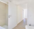 Bathroom with white tiles, glass shower, white sink, open door, hallway leading to another room