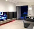 TV on the wall, couch facing TV, glass doors with view, table, lamp, table with flowers