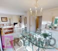 Dining room with glass table, turquoise chairs, white kitchen, chandelier, bookshelves, mirror, picture frame