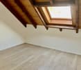 An attic with wooden beams, windows, laminate floor, and white walls.