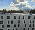 A large grey building with numerous windows, set amidst a scenic view of a city skyline and mountains in the background, solar panels installed on the roof.
