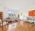 Wooden parquet floor, couch, two glass tables, chair, art paintings, window with view, wooden cabinet