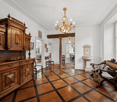 elaborate wooden furniture, hardwood floor with black trim, chandelier, wooden bench, radiator, windows