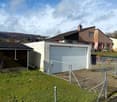 Detached house with a garage in front, surrounded by a fence, with a grassy area and a mountain in the background.