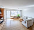 living room with wooden floor, white walls, large windows, balcony, couch, coffee table, TV cabinet, plants