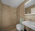 Modern, beige tiled walls, glass enclosure shower, white toilet, large mirror, white sink, silver faucet