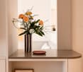 A room with a table featuring a vase with flowers, a decorative plate and picture frame underneath.