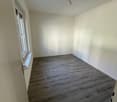 Empty room with white walls, wooden floor, window with sill, and a door.