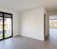 Empty room with gray floor, large windows, open doors, balcony with garden view