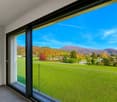 Balcony with floor to ceiling windows, sliding doors, view of wide grassy field, mountains in the distance.