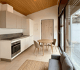 modern open plan kitchen, dining area, and living space with white cabinetry, granite countertops, large windows, wooden dining table, and a gray sofa